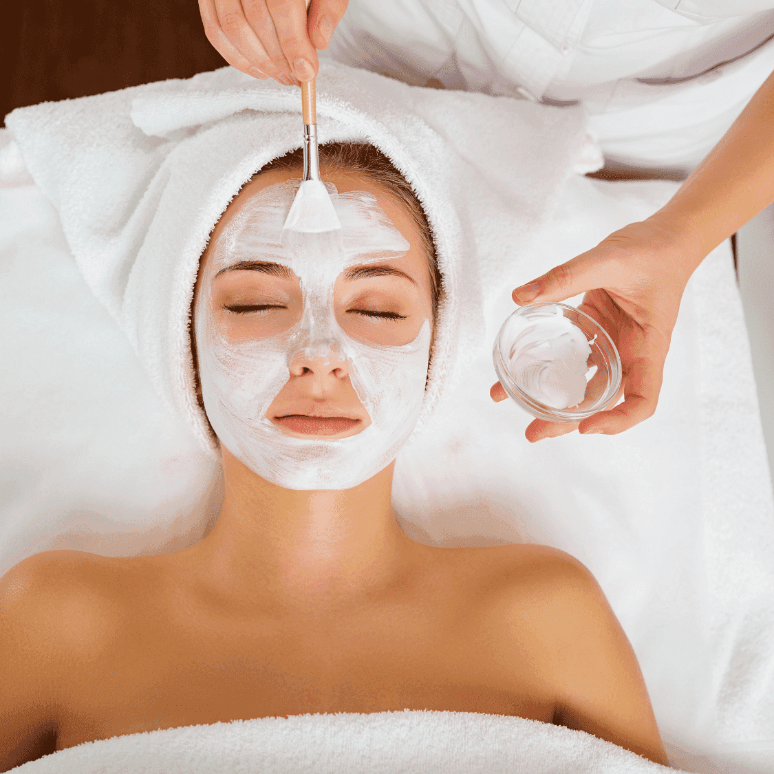Woman receiving a facial treatment with a mask applied by an aesthetician in a spa.