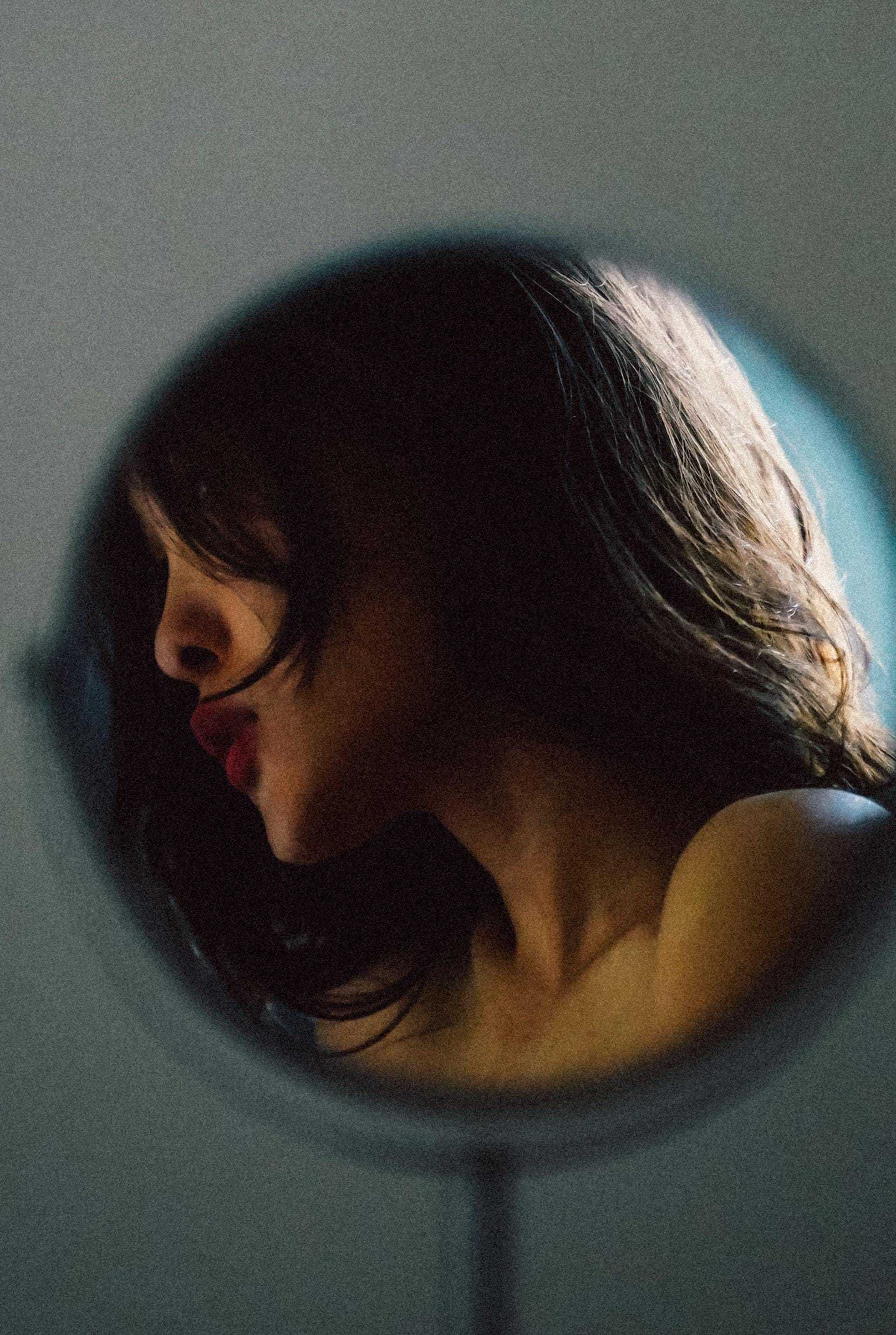 Reflection of a woman with long hair and red lips in a circular mirror.