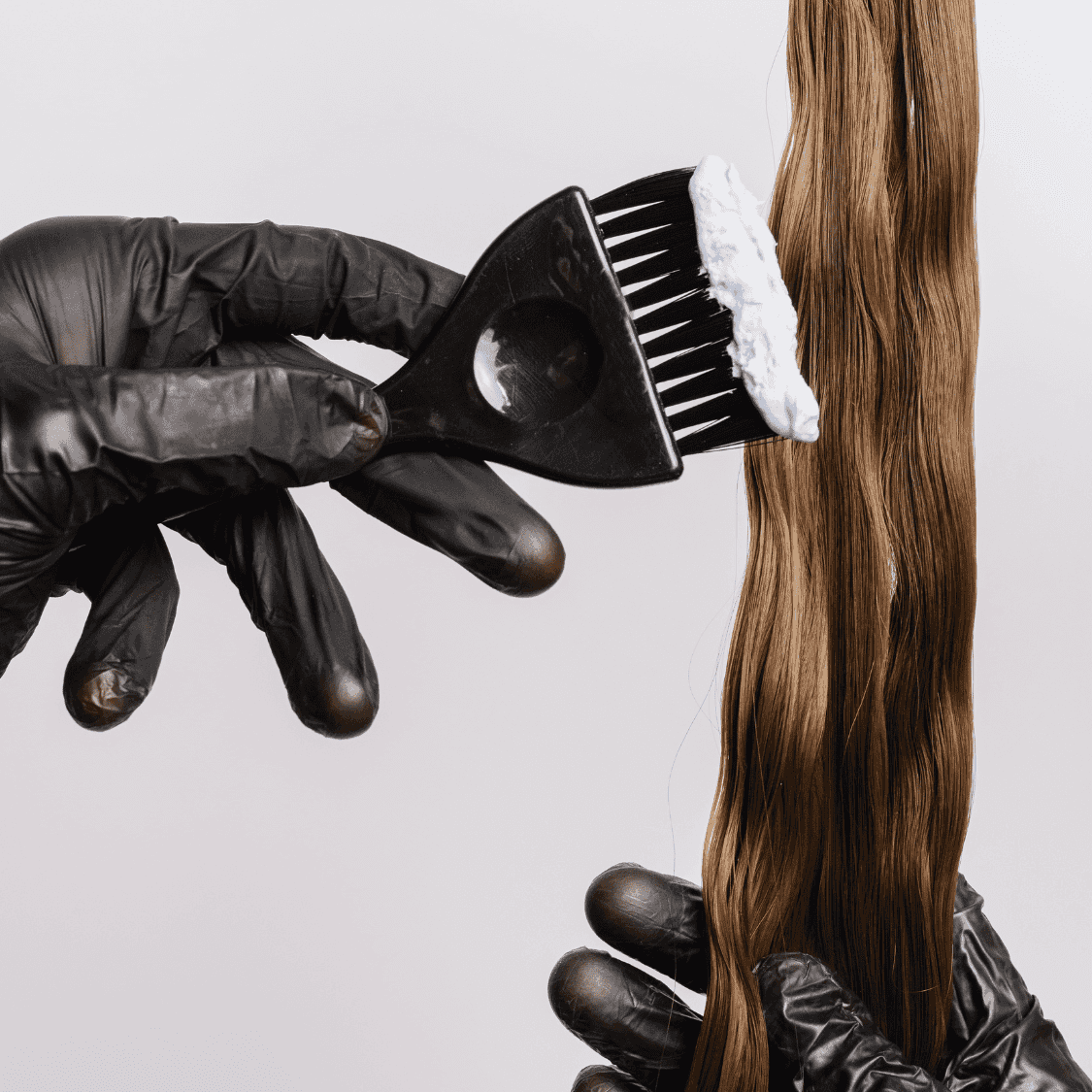 Applying hair dye to brown hair using a brush, with hands in black gloves.