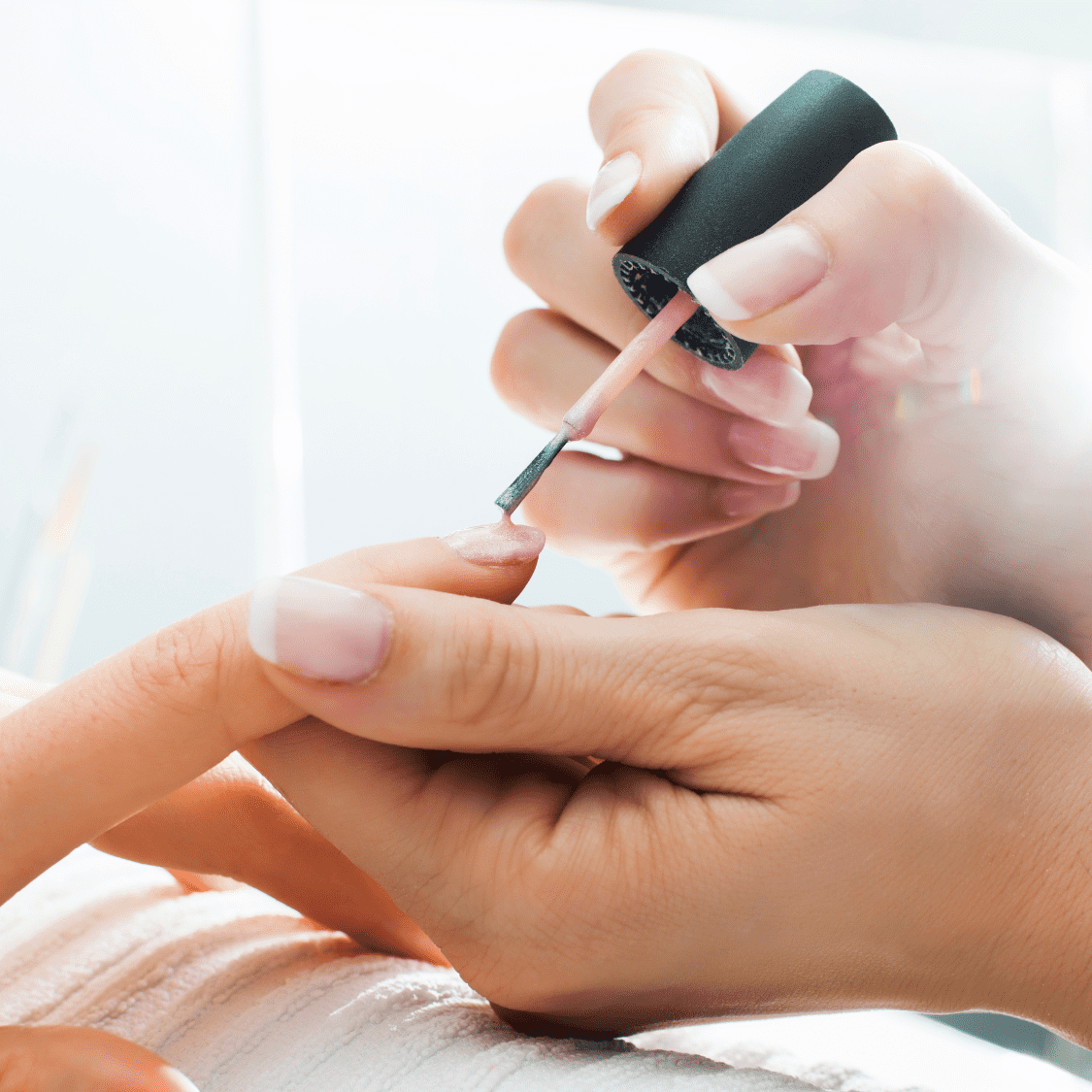 Person applying clear nail polish on someone's fingernail in a manicure session.