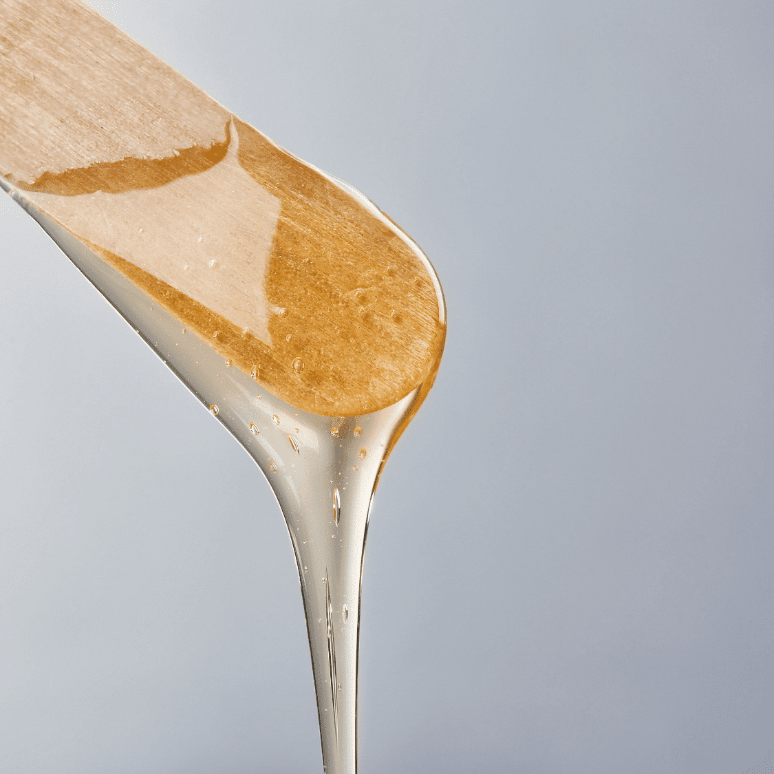 Wooden spatula with honey dripping against a light gray background.